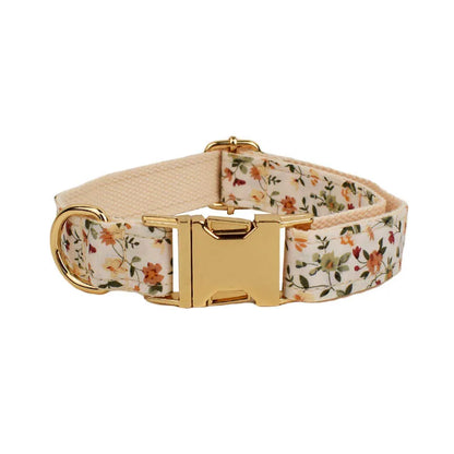Small white flower patterned dog collar, leash, vest, bow, and poop bag holder set laid out flat.