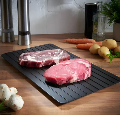 Black aluminium fast defrosting tray for kitchen use, shown thawing frozen meat.