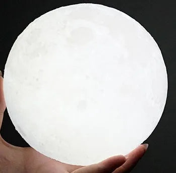 3D printed white moon lamp on wooden stand with textured lunar surface, glowing with warm yellow LED light.
