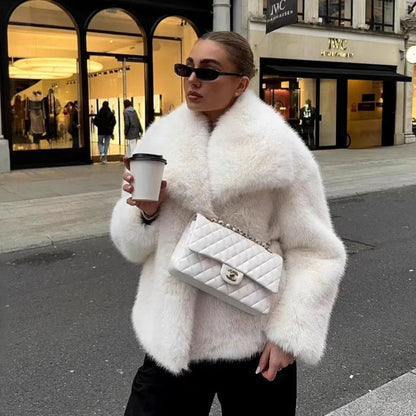 Women's white artificial fur coat with large lapel, long sleeves, and deep pockets shown in street fashion setting