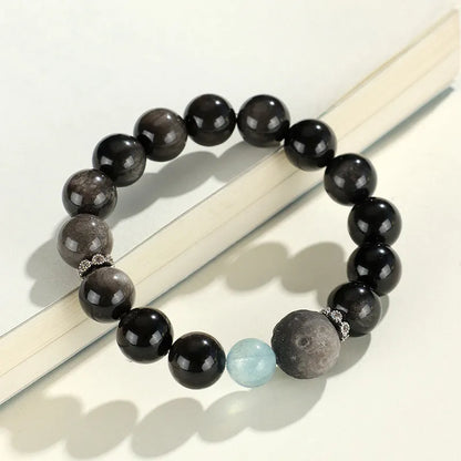 Silver stone crystal bracelet with diamond-shaped fox, cat head, and planet charms on white background.