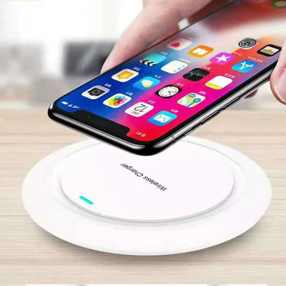 Round white wireless charging pad on desk next to mobile phone