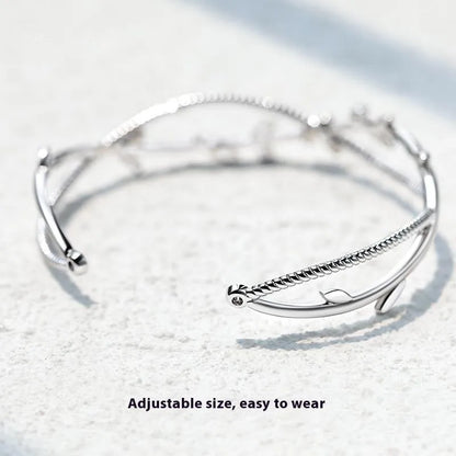 Close-up of a white gold coloured twisted copper bracelet with a branch and sprout design.