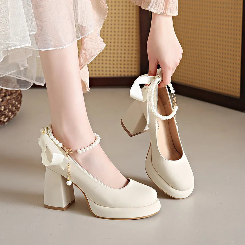 Women's beige Mary Jane shoes with chunky heel, ankle strap, pearl buckle, and round toe on a rubber sole.