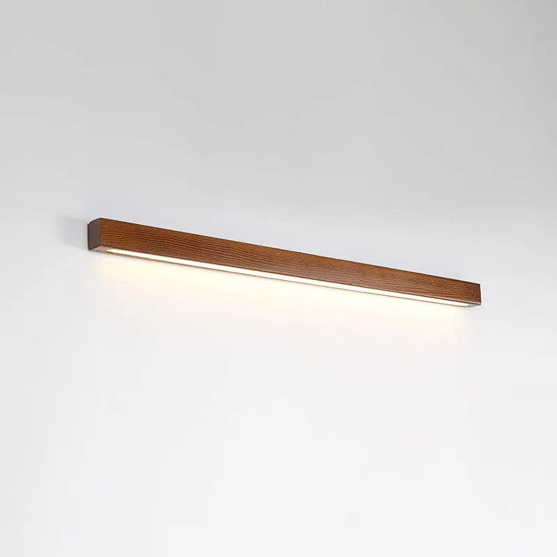 Walnut-coloured minimalist wooden strip wall lamp with integrated LEDs, mounted on a plain wall.