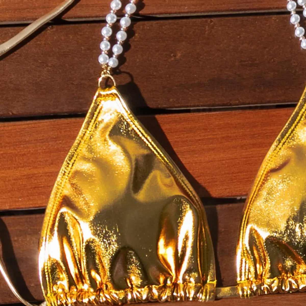 Gold women's halter neck bikini with lace-up front and pearl chain decoration on a solid background.