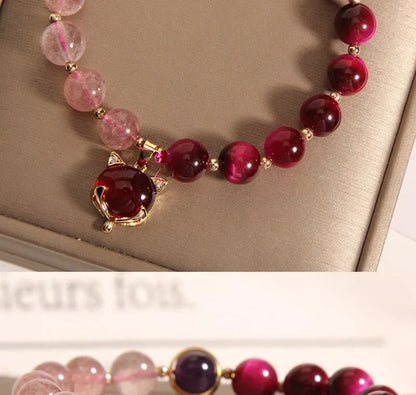 Simple women's bracelet with a red strawberry crystal charm on a black elastic rope.