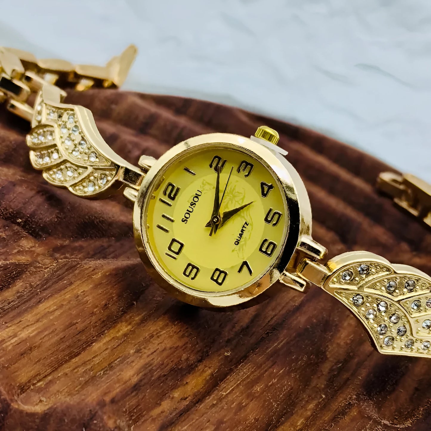 Round stainless steel women's watch on wrist showing gold surface colour and vachette clasp buckle.