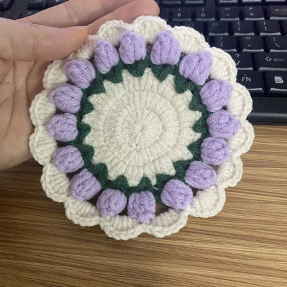 Handmade woven flower coaster in cotton and linen on a wooden table.