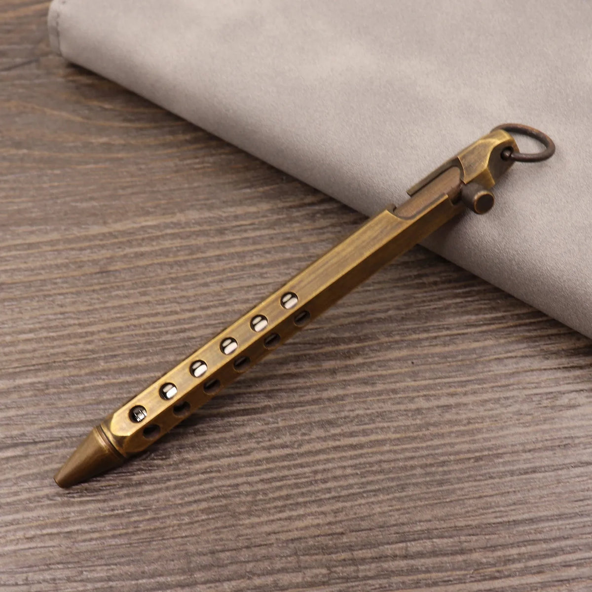 Brass tactical pen with press bolt mechanism showing cylindrical design and six ring details