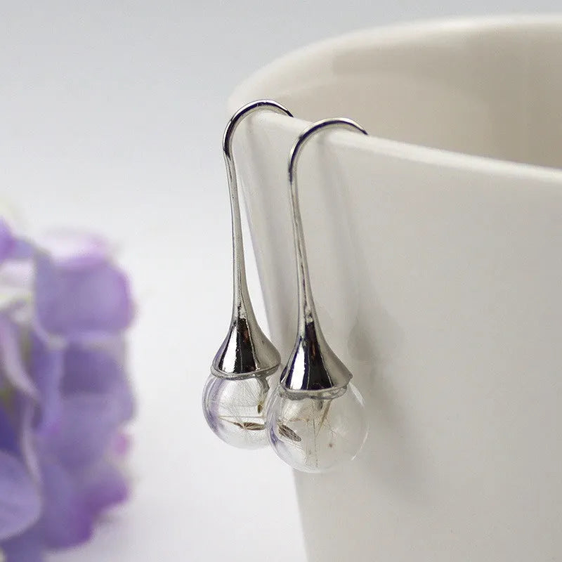 Close-up of a transparent 16mm glass ball earring with a dandelion seed inside, on a silver French hook.