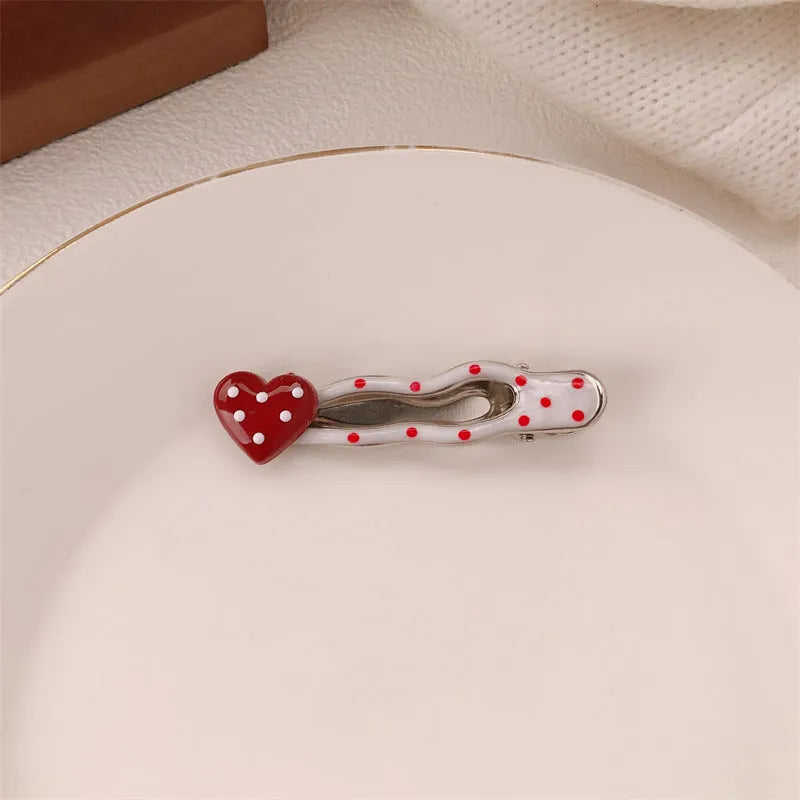 Red plastic hair clip with a 3D love heart and dots on a willow leaf-shaped base.