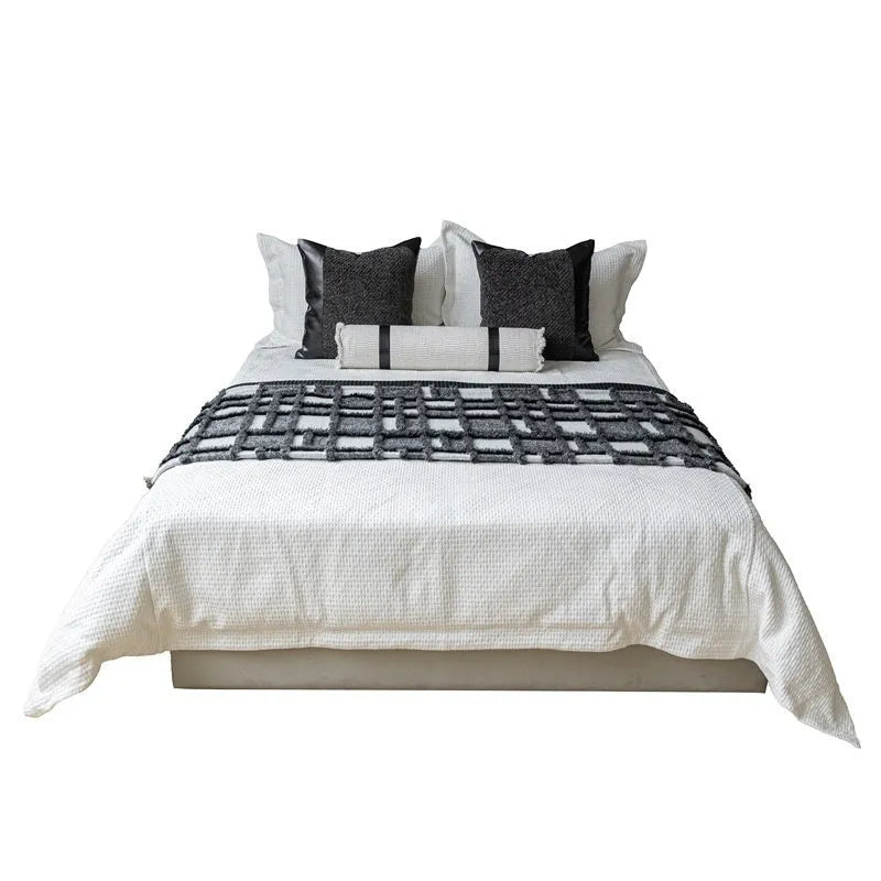 Grey and white plaid bed runner blanket with coordinating pillowcase and round leather pillow on bed