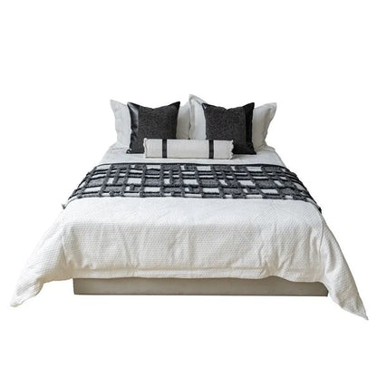 Grey and white plaid bed runner blanket with coordinating pillowcase and round leather pillow on bed