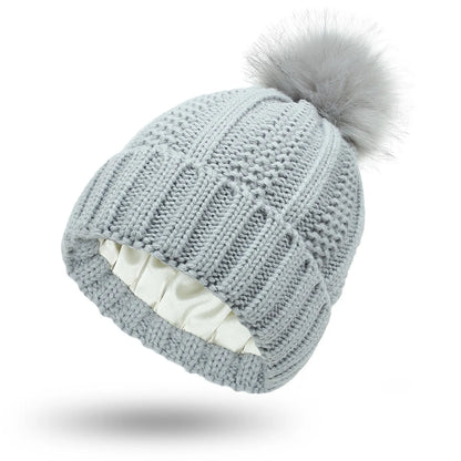 Wool knit beanie hat for women with faux fur pom pom and satin lining, shown in a wine red colour.