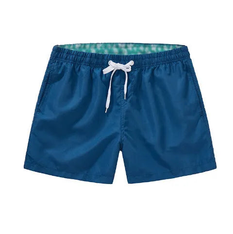 Man wearing straight-leg polyester beach shorts in a bright colour on the sand.