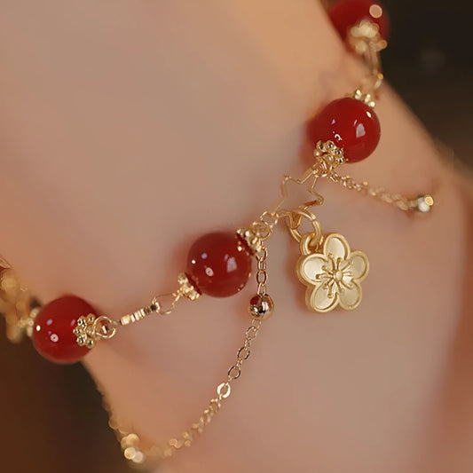 Red agate double layer bracelet with flower and peach blossom charms on a wrist.