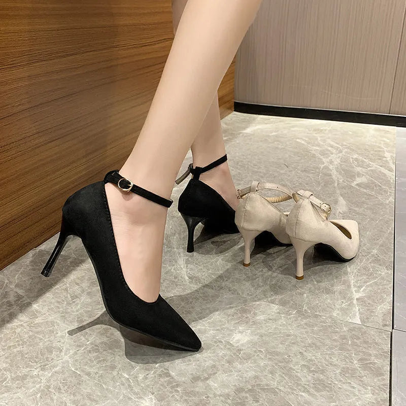 Women's black stiletto heels with skull pattern and ankle buckle closure on wooden floor