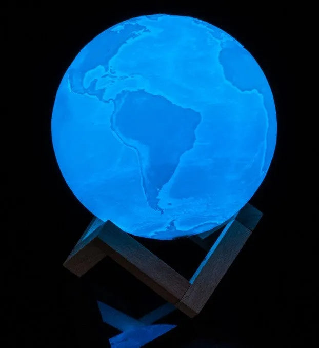 3D printed white moon lamp glowing on a wooden stand, showing detailed crater texture on its surface.