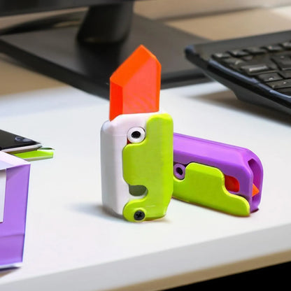Small orange and green 3D printed plastic carrot knife fidget toy with blade extended.
