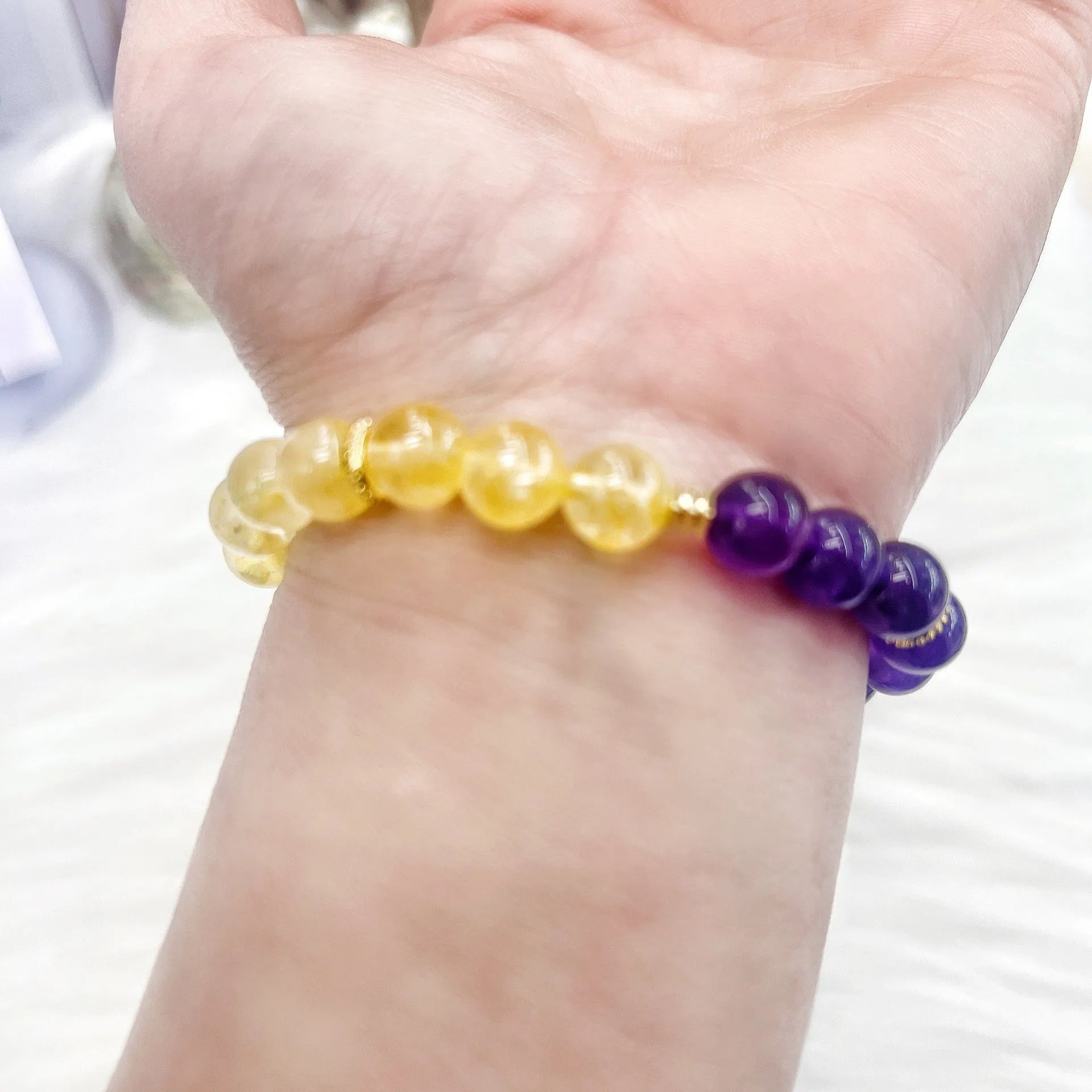 Handmade women's crystal bracelet in yellow and purple colours on a wrist.