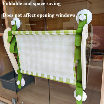 Pink cat hammock with wooden frame and suction cups attached to a window, with a cat resting inside.