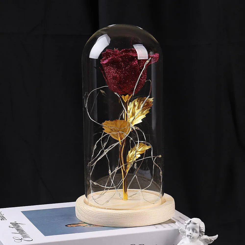 Red eternal rose flower arrangement with LED lights inside a glass dome on a table.