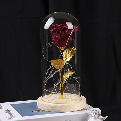 Red eternal rose flower arrangement with LED lights inside a glass dome on a table.