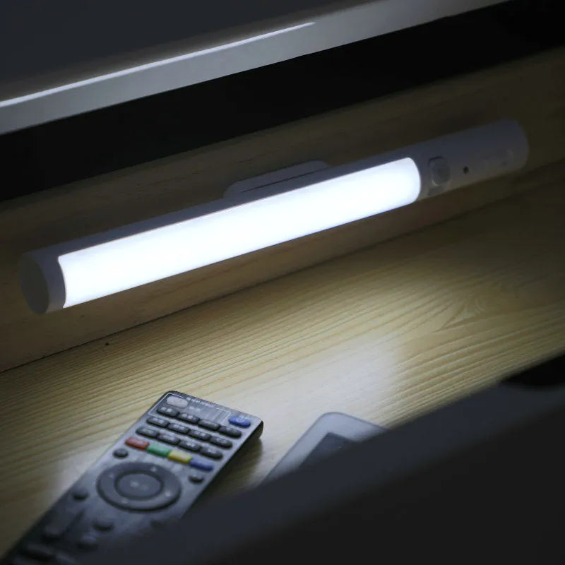 Slender white human body induction LED cabinet light with magnetic back for tool-free installation.