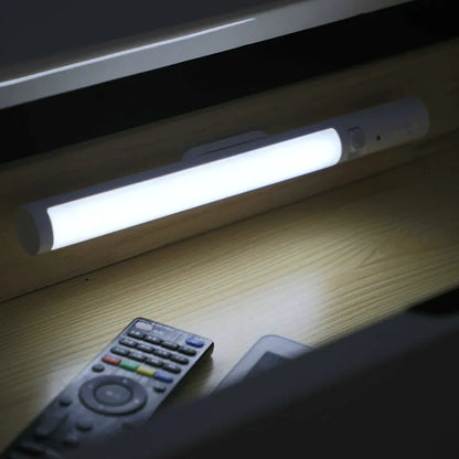 Slender white human body induction LED cabinet light with magnetic back for tool-free installation.