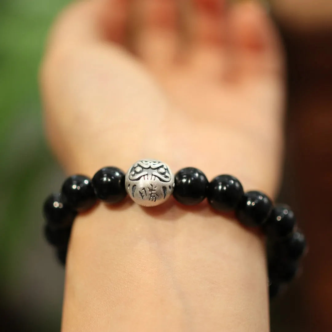 A bracelet with large black agate beads and a sterling silver clasp on a wrist.