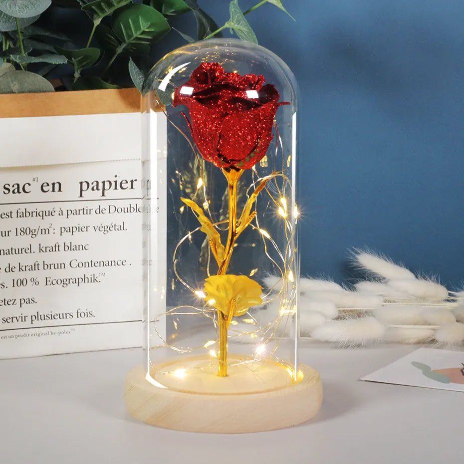 Red eternal rose flower arrangement with LED lights inside a glass dome on a table.
