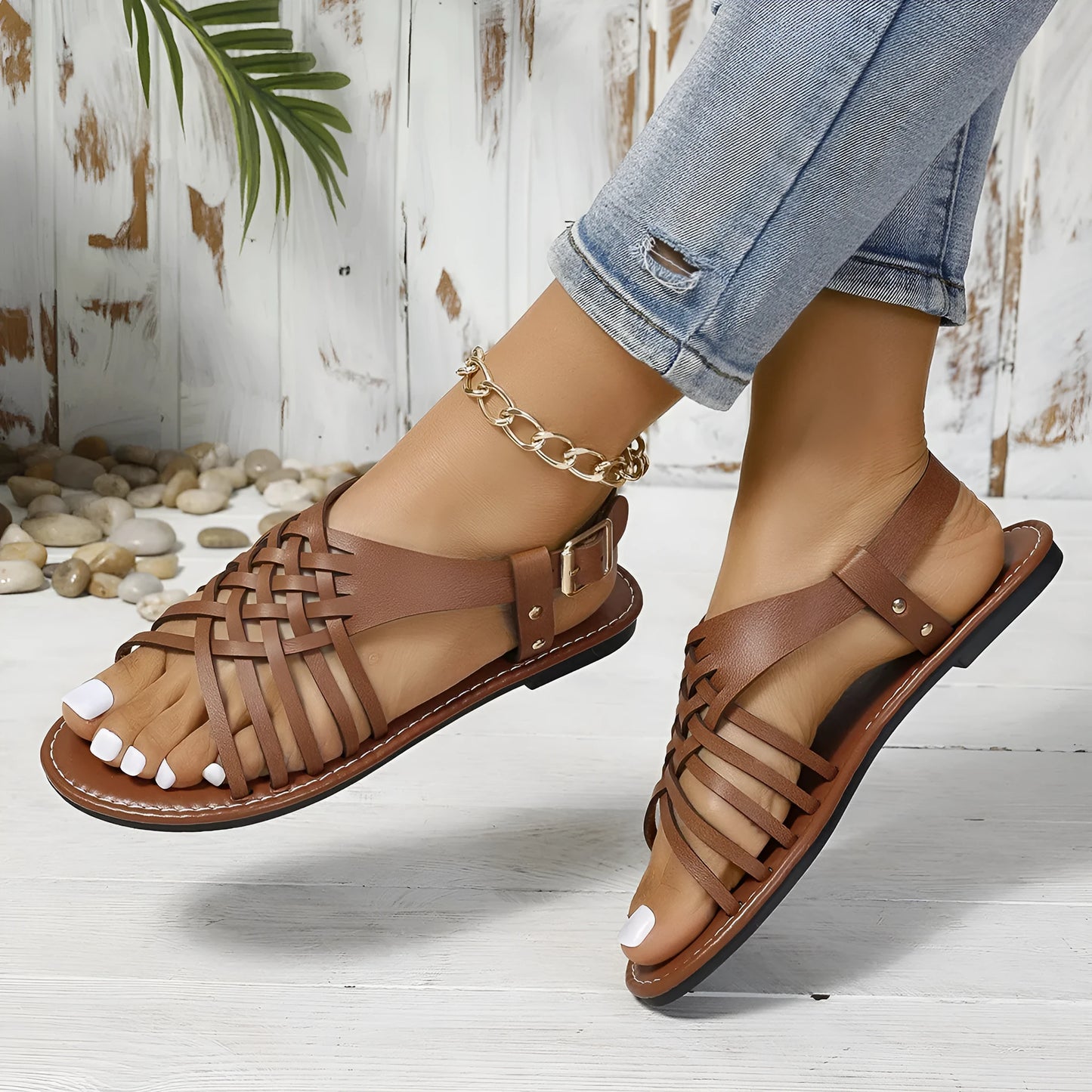 Black Roman style beach slippers with cross straps and buckle fastening on wooden floor