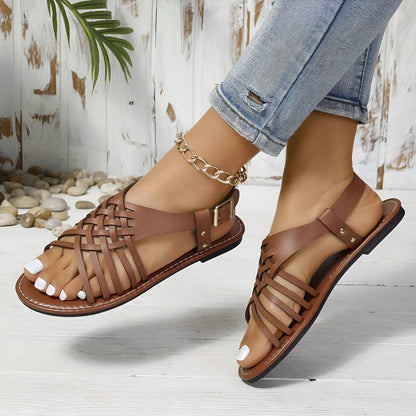 Black Roman style beach slippers with cross straps and buckle fastening on wooden floor