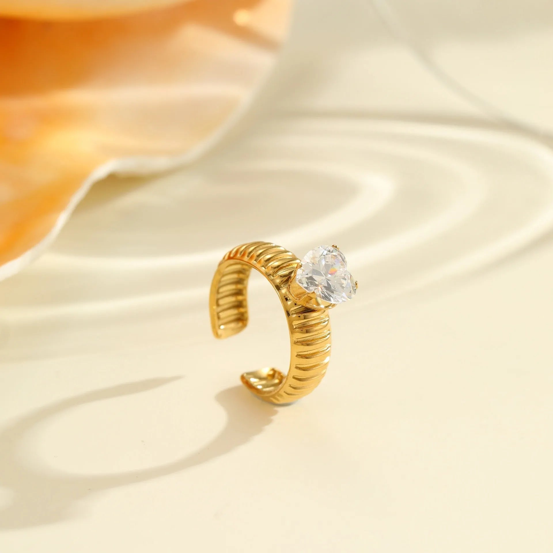 Gold electroplated stainless steel open mouth ring with geometric shapes and zircon inlay on a heart drop.