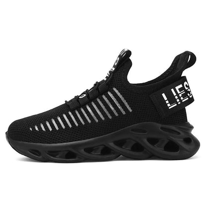 Children's black fabric sneakers with a Velcro strap and patterned EVA sole on a wooden floor.
