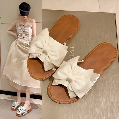 Women's beige suede slip-on sandals with a flat rubber sole and decorative bow.