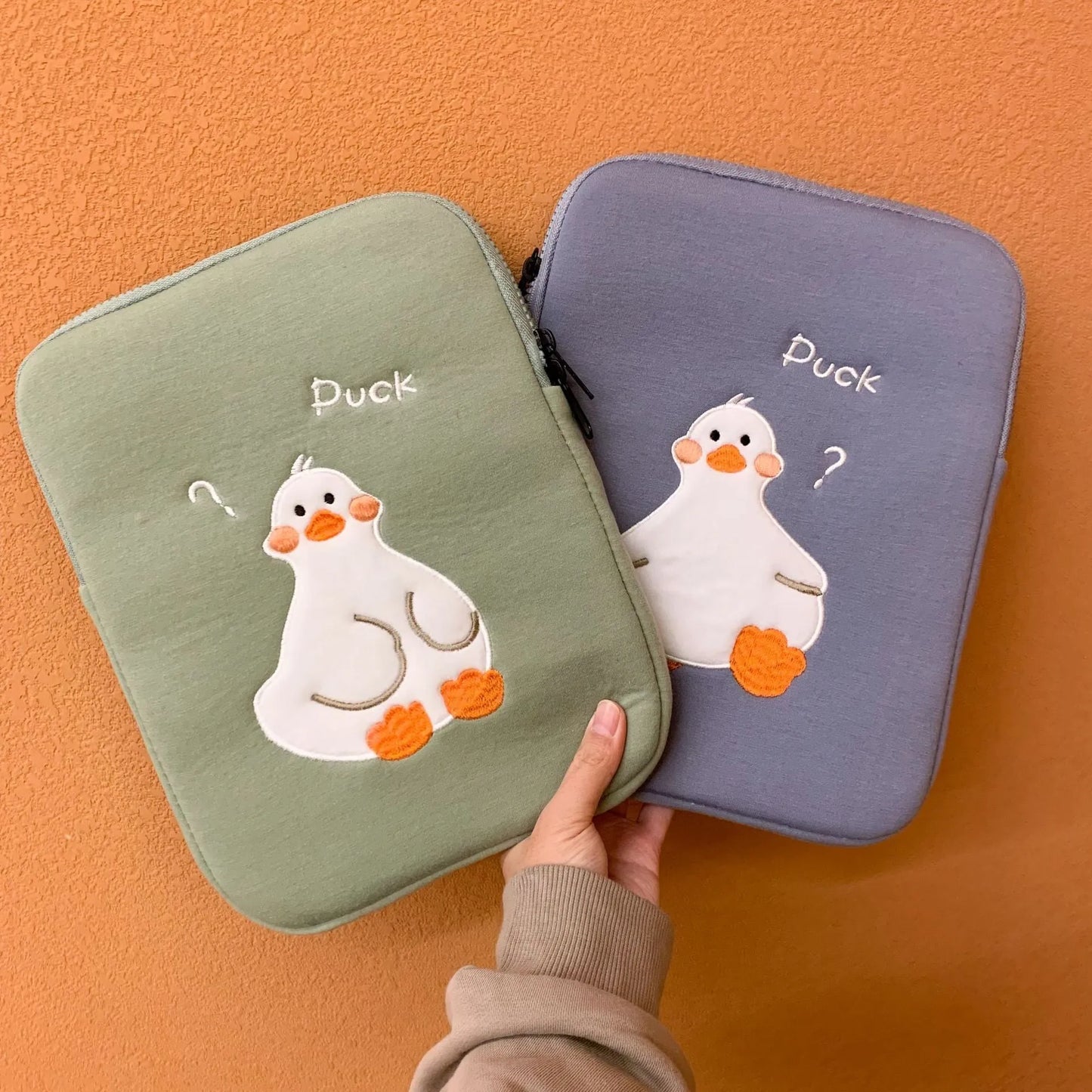 Blue tablet case with embroidered cartoon duck design showing zipper closure and cotton fabric texture