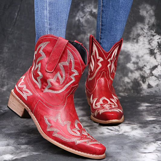 Women's blue embroidered cowboy ankle boots with a low wedge heel and pointed toe on a wooden floor.
