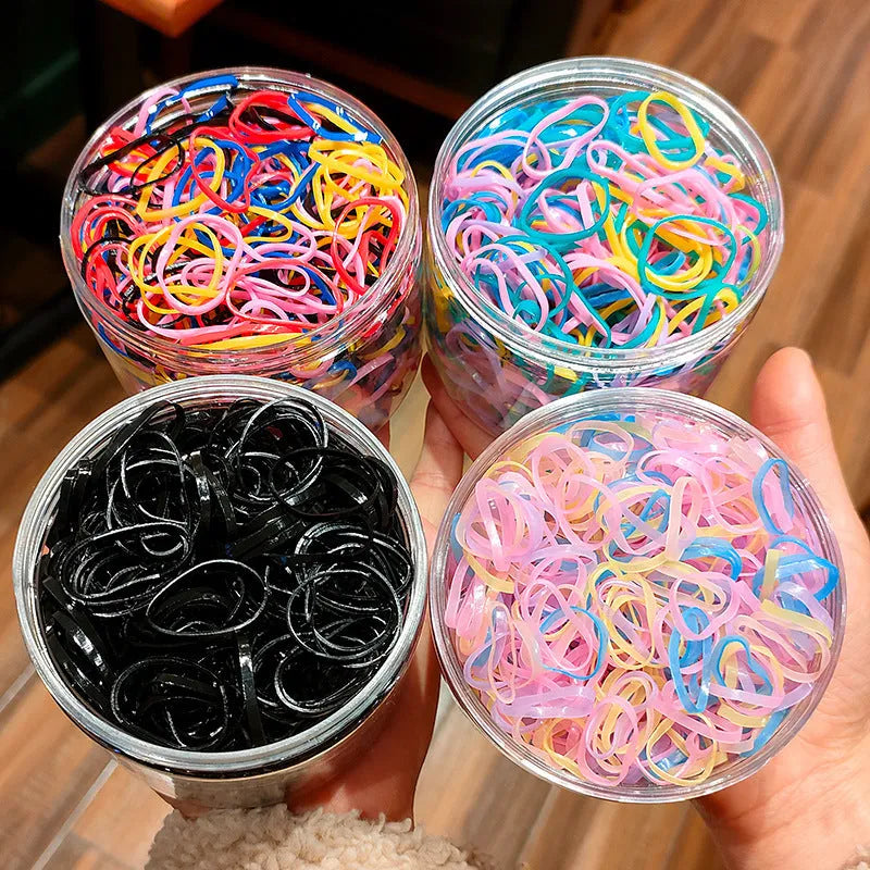 Multicoloured assortment of thin TPU elastic hair bands for babies and children in a reusable plastic container.