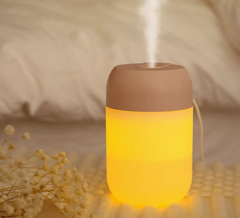 White cylindrical humidifier with USB cable on a desk, showing compact 15cm height and aromatherapy function for essential oils.