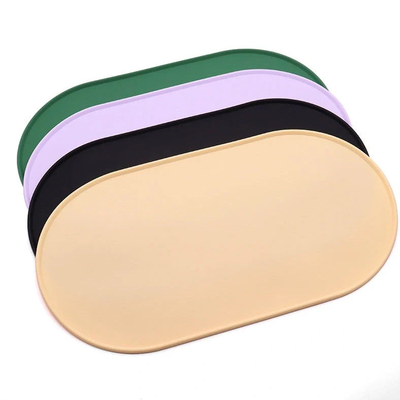 Green silicone cat feeding placemat with raised edges on wooden floor containing water bowl