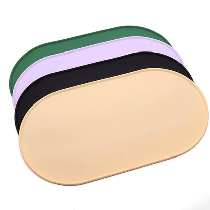 Green silicone cat feeding placemat with raised edges on wooden floor containing water bowl