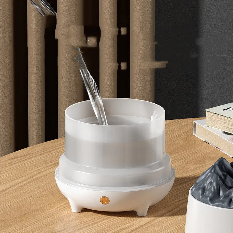 White volcano-shaped humidifier with USB cable on a wooden table, emitting mist.