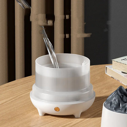 White volcano-shaped humidifier with USB cable on a wooden table, emitting mist.
