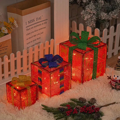 Set of three sparkling LED-lit Christmas gift boxes with red bows on a snowy porch.