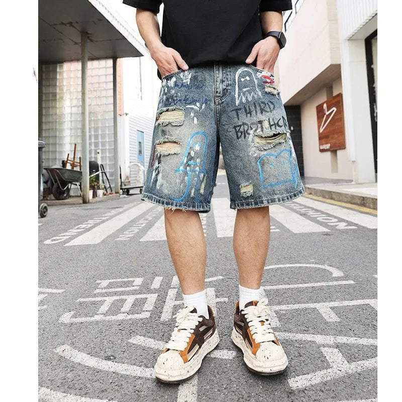 Blue denim men's shorts with ripped knees and graffiti design, featuring a straight leg and zipper fly.