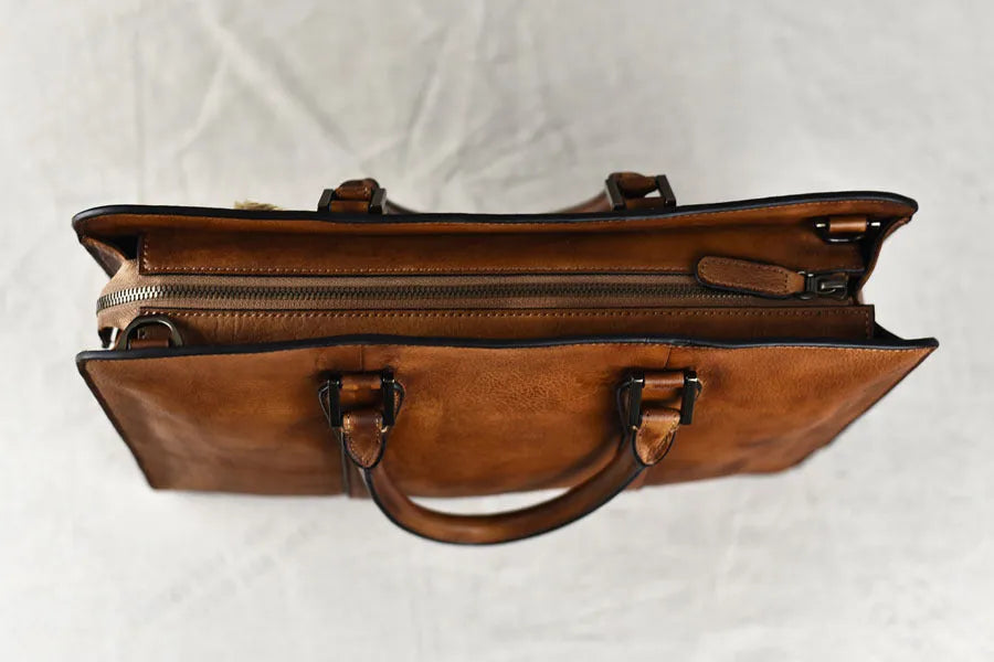 Khaki men's retro leather handbag with a horizontal square shape and top zipper, shown on a table.