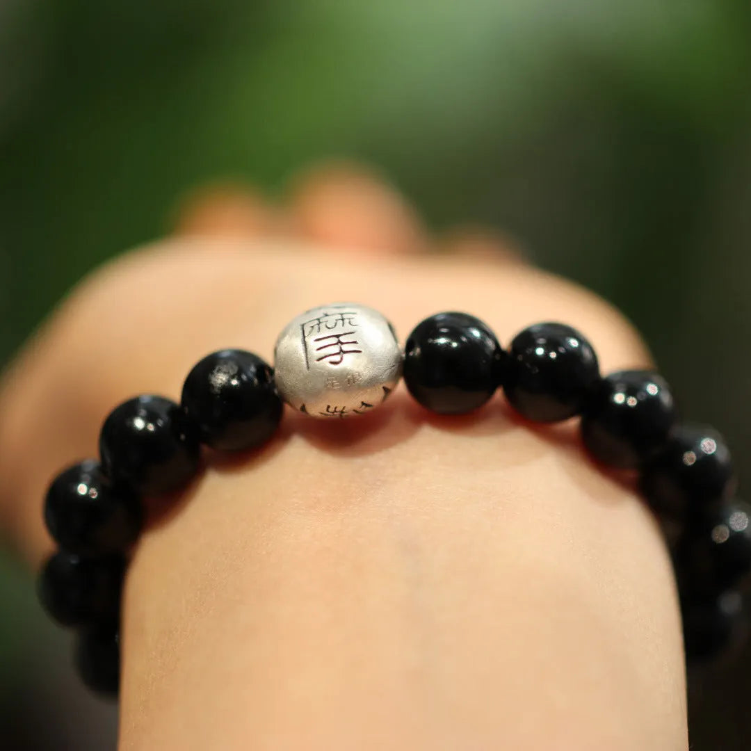 A bracelet with large black agate beads and a sterling silver clasp on a wrist.
