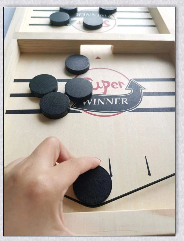 Two players competing in a wooden hockey game with pucks flying across the table